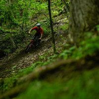 Mountain biker in red making a left turn along an off-cambered trail. 