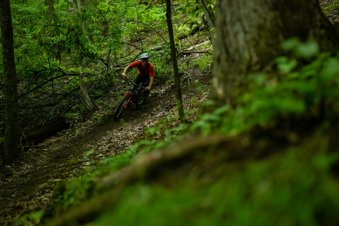 Mountain biker in red making a left turn along an off-cambered trail. 